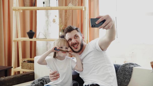 Portrait of a little blonde daughter and her father, have moustache made of hair. Take a selfie. Father day - Photo, image
