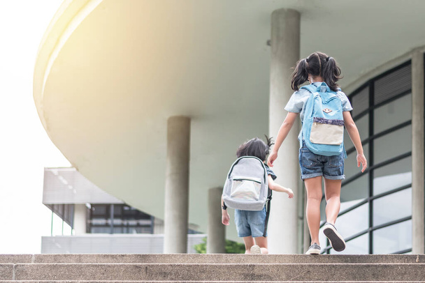 Back to school education concept with girl kids (elementary students) carrying backpacks going, running to class on school first day and walking up building stair happily - Photo, Image