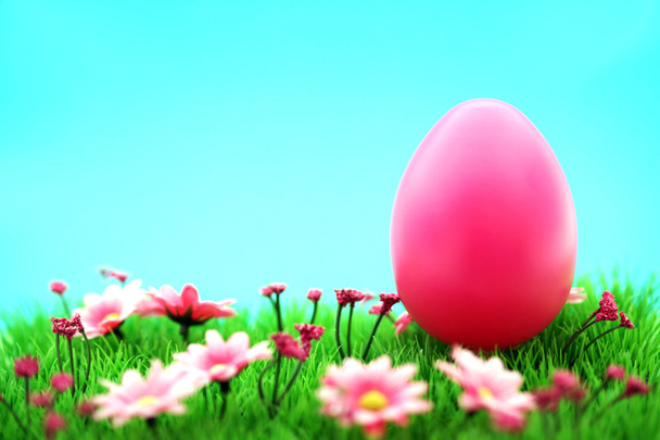 Рожеве пасхальне яйце на лузі з квітами та блакитним фоном
 - Фото, зображення