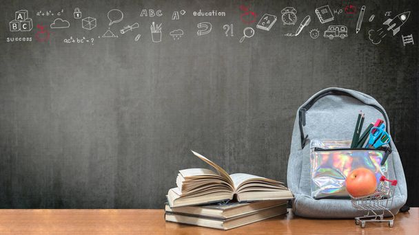 Back to school concept with school books, textbooks, backpack and stationery supplies on classroom desk with teacher's black chalkboard background with educational doodle for new academic year begin  - Photo, Image