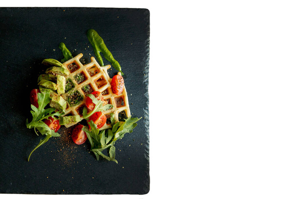 Fresh baked Belgian waffles with arugula, tomatoes and avocado on black a plate isolated on white background. Savory waffles. Breakfast concept. Healthy breakfast. - Foto, Bild
