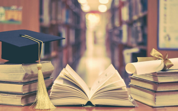 Sukces edukacyjny z kapeluszem dyplomowym, czapką akademicką, moździerzem i dyplomem z książek i podręczników w klasie lub bibliotece - Zdjęcie, obraz