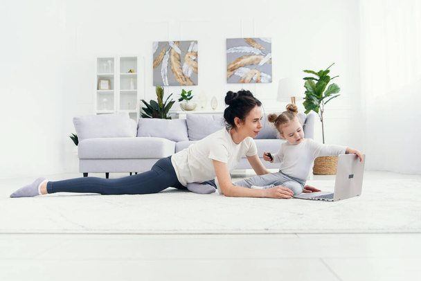 Young mother and her adorable daughter are using laptop while lying on the floor. - Foto, Bild