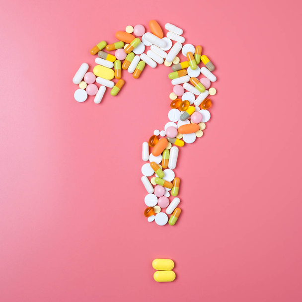 Primer plano de muchas píldoras diferentes en forma de signo de interrogación sobre fondo rosa
. - Foto, imagen