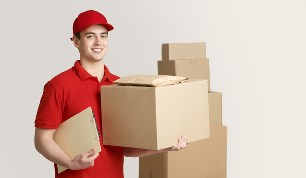 Courier and package in warehouse. Deliveryman holding box and tablet near stack of parcels - Fotoğraf, Görsel