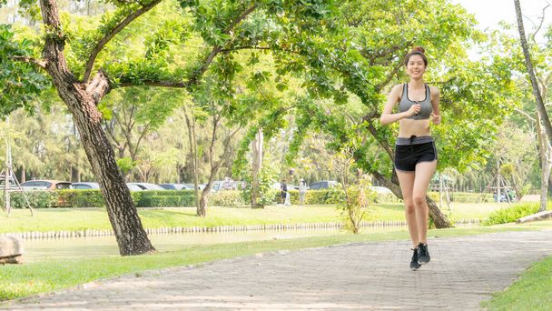 Aziatisch vrij slank meisje in de mode sportkleding loopt in de openbare tuin ochtend. Concept joggen buiten in hun steden. - Foto, afbeelding