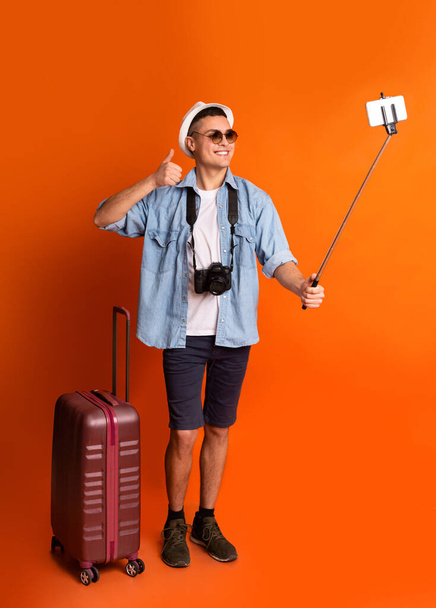 Traveler with suitcase taking selfies over orange background - Foto, Imagem