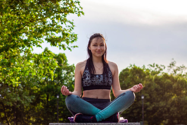 Beautiful   brunette girl is  doing yoga Easy Pose Sukhasana in the park.  Concept of sport    - Photo, Image