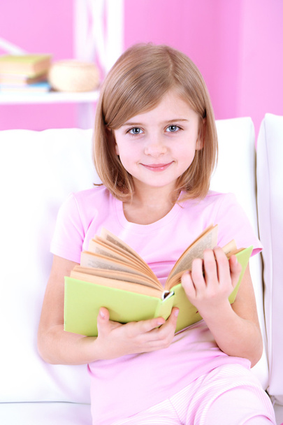 Little girl reading book sitting on sofa in room - Foto, imagen