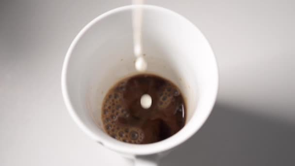 Powolny ruch mleka spada na kawę napełniając filiżankę do kawy z mlekiem - Materiał filmowy, wideo