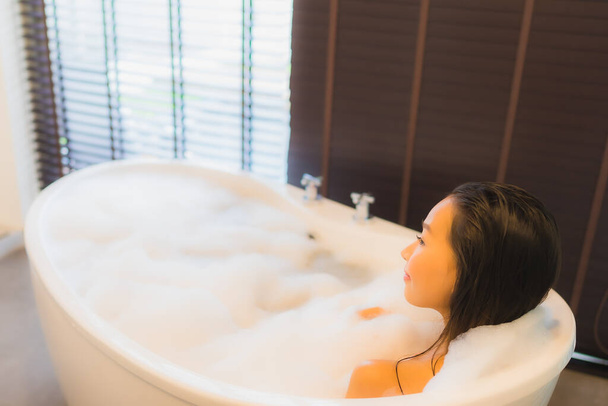 Portret mooie jonge aziatische vrouw gelukkig glimlach ontspannen neem een bad in bad van badkamer interieur - Foto, afbeelding