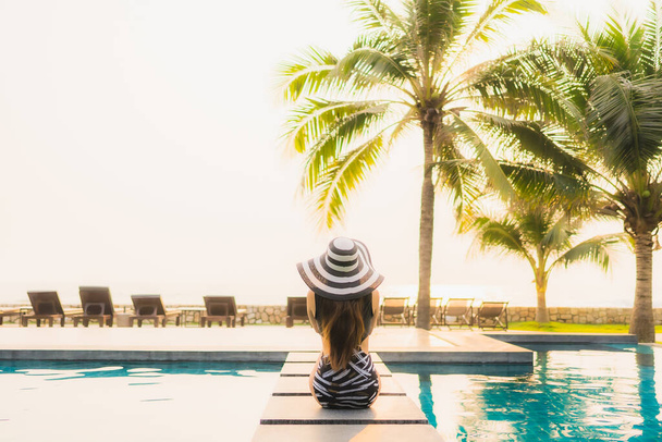 Portrait beautiful young asian woman relax around outdoor swimming pool in hotel resort with palm tree at sunset or sunrise for leisure vacation - Photo, Image