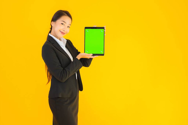 Портрет красива молода азіатка щаслива посмішка з пристроєм розумних планшетів на жовтому ізольованому фоні
 - Фото, зображення