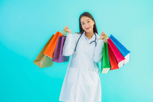 Portret mooie jonge aziatische arts vrouw met kleurrijke boodschappentas van winkelcentrum op blauwe geïsoleerde achtergrond - Foto, afbeelding