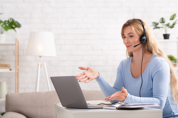 Memleketten bir müşteriyle iletişim. Kulaklıklı ve dizüstü bilgisayarlı bir kadın masada oturuyor. - Fotoğraf, Görsel