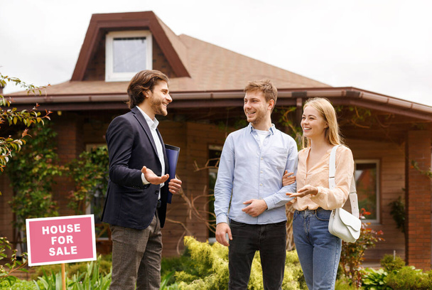 Young family talking to real estate agent about purchasing property near beautiful house outside - Photo, Image
