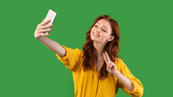 緑の背景にセルフィーを作るスマートフォンを使用してティーンの女の子,パノラマ - 写真・画像