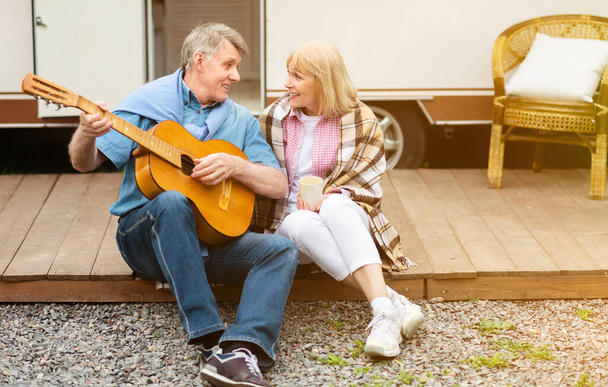 Beau vieil homme avec guitare chantant à sa douce femme près de leur véhicule de loisirs à l'extérieur
 - Photo, image