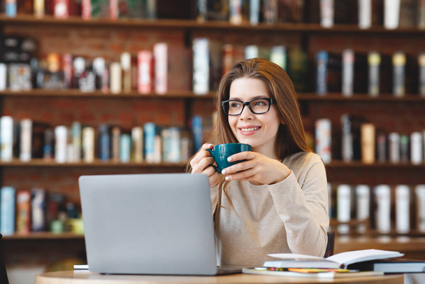 Szczęśliwa młoda dziewczyna pracuje na laptopie, siedzi w kawiarni - Zdjęcie, obraz