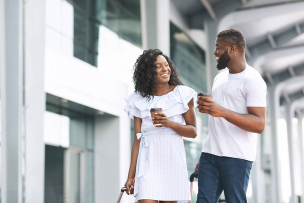 Glückliche schwarze Männer und Frauen, die mit Kaffee in der Nähe des Flughafengebäudes spazieren gehen - Foto, Bild