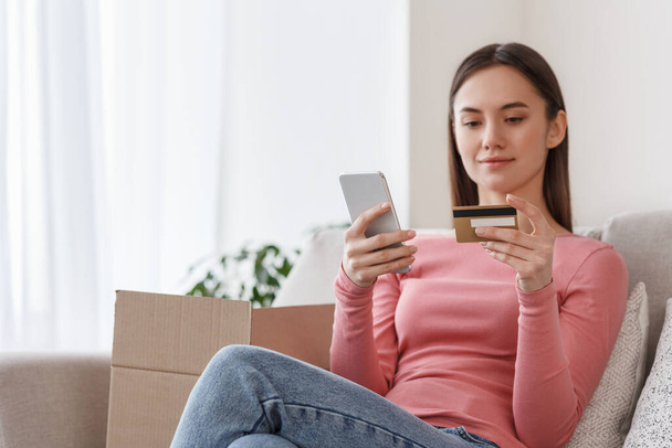 Ordine rapido dal negozio online. Ragazza con smartphone e carta di credito si siede sul divano con scatole di cartone
 - Foto, immagini