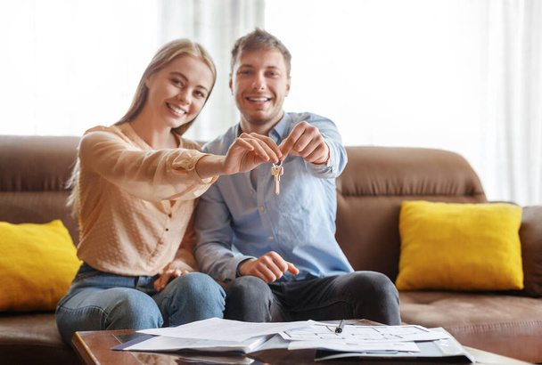 Beautiful millennial girl with her happy boyfriend holding key to their new house indoors - Photo, Image