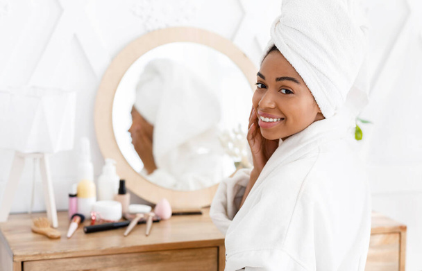 Счастливая черная девушка с полотенцем на голове сидит за туалетным столиком
 - Фото, изображение