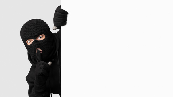 Maskovaný zloděj vykukuje z bílého prázdného prkna a dělá ceduli - Fotografie, Obrázek