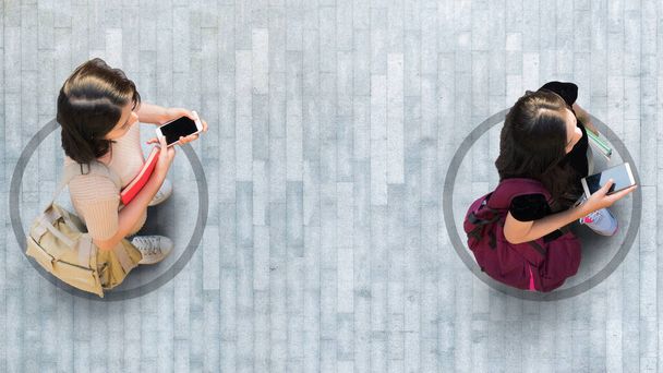 Ανθρώπινη ζωή σε κοινωνική απόσταση. Αεροφωτογραφία με δύο φοιτήτριες με smartphone stand σε γκρι πεζοδρόμιο δρόμο με άδειο χώρο. - Φωτογραφία, εικόνα