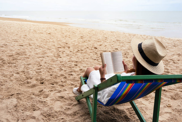 Egy gyönyörű nő fekszik és könyvet olvas a tengerparti széken, nyugodt érzéssel. - Fotó, kép