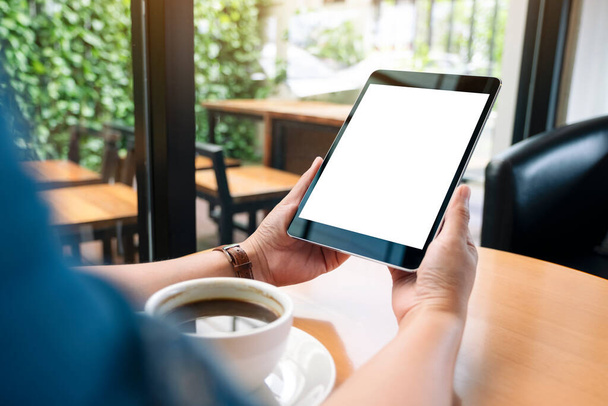 Макетне зображення рук, що тримають чорний планшетний ПК з порожнім білим екраном з чашкою кави на дерев'яному столі
  - Фото, зображення