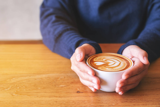 Imagen de una mujer sosteniendo una taza de café caliente sobre una mesa de madera - Foto, imagen