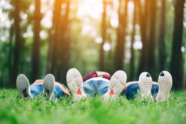 Füße einer Gruppe junger Leute im Liegen auf einem grünen Gras im Wald - Foto, Bild