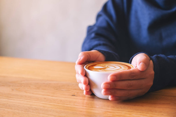 Image rapprochée d'une femme tenant une tasse de café chaud sur une table en bois - Photo, image