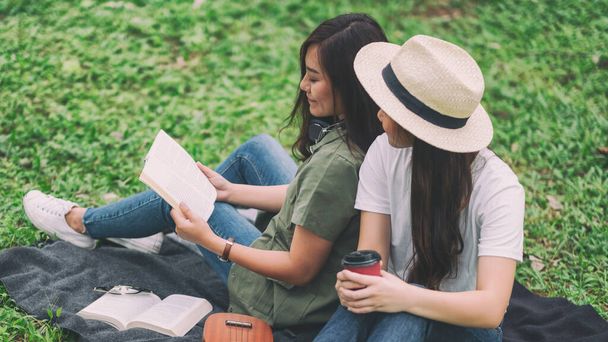 Δύο γυναίκες διαβάζουν μαζί το βιβλίο ενώ κάθονται στο δάσος. - Φωτογραφία, εικόνα