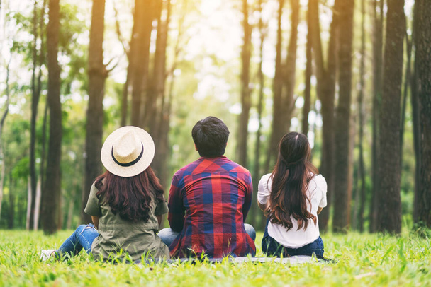 Группа путешественников, сидящих на зеленой траве и смотрящих в красивый сосновый лес
 - Фото, изображение