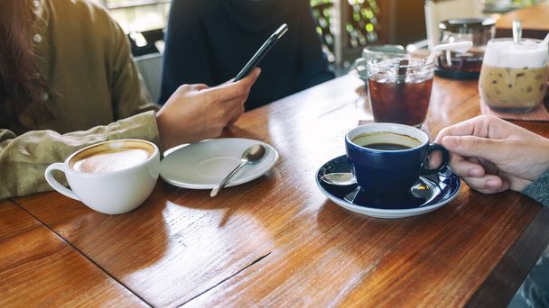 Imagem de perto de pessoas usando telefone celular e beber café juntos no café - Foto, Imagem