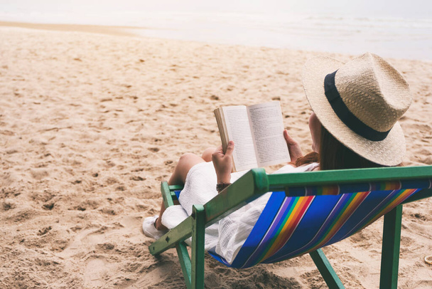 Egy gyönyörű nő fekszik és könyvet olvas a tengerparti széken, nyugodt érzéssel. - Fotó, kép