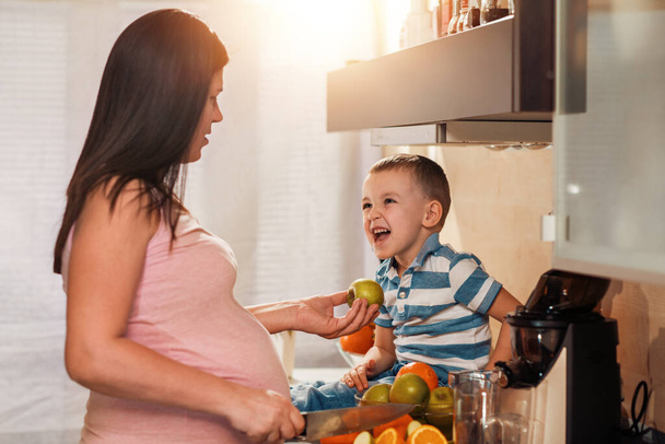 Kobieta w ciąży i jej syn przygotowują sok ze świeżych owoców. - Zdjęcie, obraz