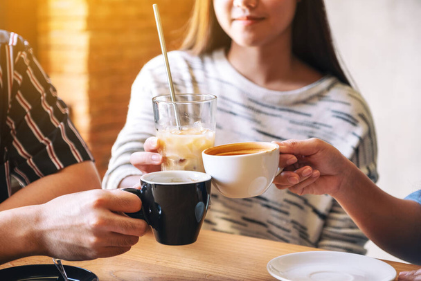 Imagen de cerca de tres personas tazas de café tintineo en la mesa de madera en la cafetería
 - Foto, imagen