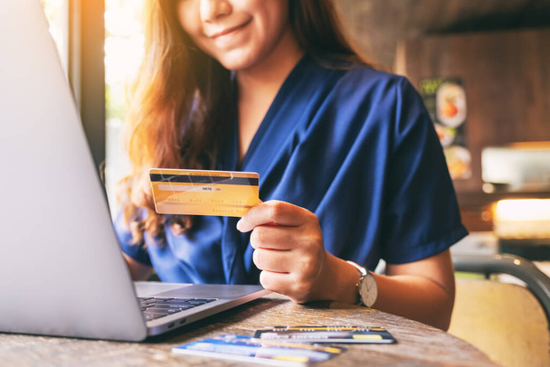 Imagen de primer plano de una mujer de negocios que sostiene la tarjeta de crédito mientras utiliza el ordenador portátil
 - Foto, imagen