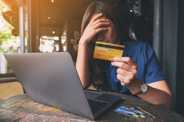 Immagine da primo piano di una donna asiatica stressata e al verde mentre tiene in mano la carta di credito con il computer portatile sul tavolo
 - Foto, immagini