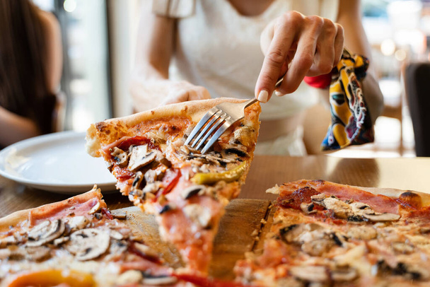 Zbliżenie na plasterek pizzy nieznane kaukaskie kobieta biorąc jedzenie z talerza w restauracji w letni dzień widok niezdrowe jedzenie - Zdjęcie, obraz