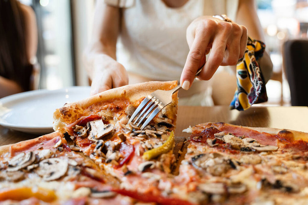 Close-up em fatia de pizza mulher caucasiana desconhecida tomando alimentos do prato no restaurante no dia de verão vista frontal alimentação insalubre
 - Foto, Imagem