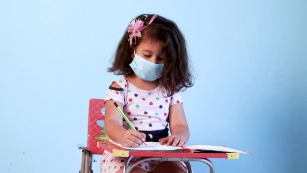 Kleines Mädchen mit Schutzmaske schreibt Schularbeiten, Schulkonzept zu Hause, während Covid-19 Lock down, Quarantäne,  - Filmmaterial, Video