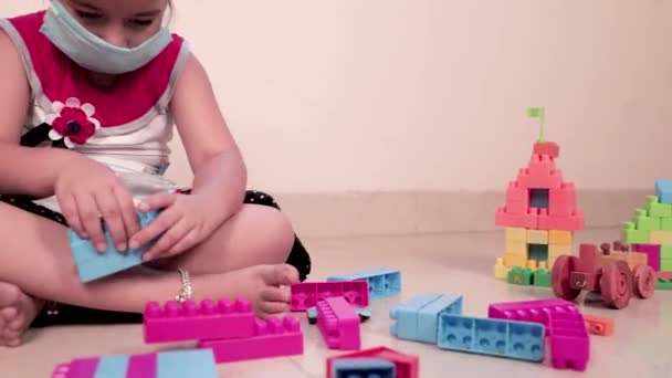Kleines Mädchen mit Maske spielt mit bunten Legowürfeln. Niedliche weibliche Kind spielen mit Plastik-Spielzeug zu Hause während der Quarantäne, Covid-19. Steadicam-Schuss. - Filmmaterial, Video
