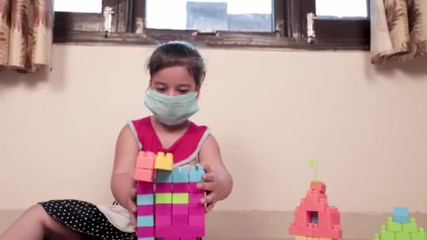 Dolly Shot van kleine meisje dragen masker spelen met kleurrijke Lego Dices. Schattig vrouwelijk kind spelen met plastic speelgoed thuis tijdens quarantaine, Covid-19.  - Video