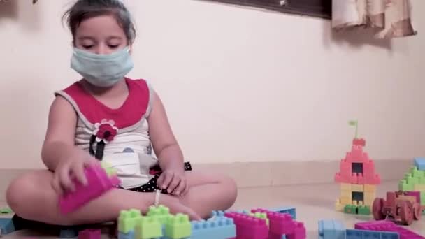 Klein meisje dragen masker spelen met kleurrijke Lego Dices. Schattig vrouwelijk kind spelen met speelgoed thuis tijdens quarantaine, Covid-19.  - Video
