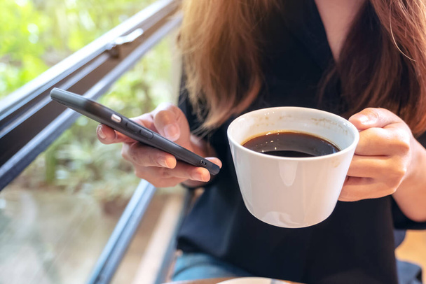 Detailní záběr ženy držící, používající a dotýkající se chytrého telefonu při pití kávy - Fotografie, Obrázek