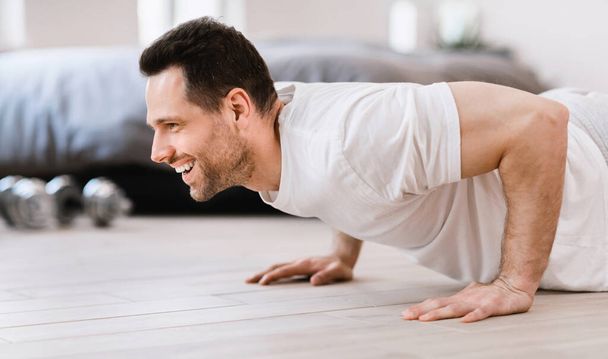 Happy Man Doing Plank Exercise Training Indoors On Weekend Morning - 写真・画像
